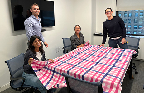 Bluestar team members working with large cloth on table to make blankets for PICU infants