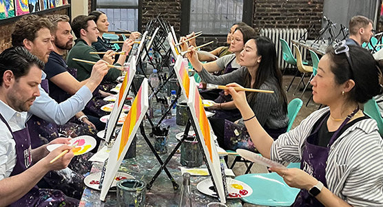 Bluestar team seated at tables, each person studiously working with brush on canvas