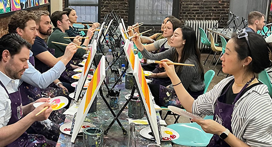 Bluestar team seated at tables, each person studiously working with brush on canvas